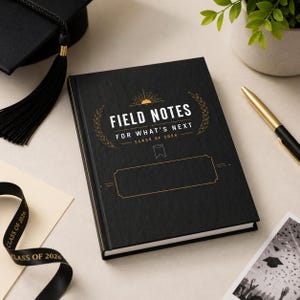 Könnte beinhalten: Ein schwarzes Notizbuch mit goldfarbenem Schriftzug "FIELD NOTES" und "FOR WHAT'S NEXT CLASS OF 2026". Das Notizbuch hat einen goldenen Rand und einen leeren Bereich für einen Namen. Eine Abschlusskappe und ein Band sind ebenfalls im Bild.