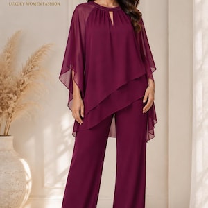 May include: A deep burgundy two-piece ensemble consisting of wide-leg trousers and a matching layered chiffon tunic top. The top features a round neckline with a small keyhole cutout, sheer cape-style sleeves, and a tiered hemline design.
