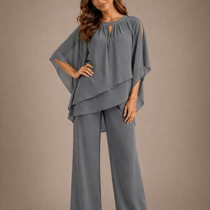 May include: A slate grey two-piece trouser suit featuring a layered, flowy chiffon tunic top with a round neckline, a small keyhole cutout, and split cape-style sleeves. The matching trousers are wide-legged and floor-length, creating a cohesive look.