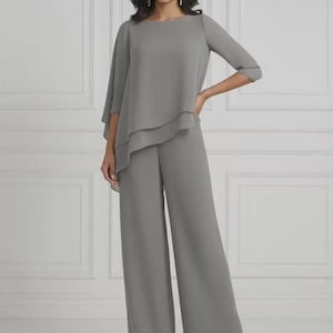 May include: A two-piece grey outfit comprising a layered top with short sleeves and wide-leg trousers. The top has a round neckline and a flowing, layered design. The trousers are floor-length and have a relaxed fit. The outfit is made of a lightweight fabric.