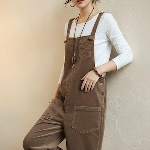 May include: Brown corduroy overalls with large front pockets and adjustable straps. The overalls have a relaxed fit and are paired with a white long-sleeved shirt. The overall design is casual and comfortable, suitable for everyday wear.