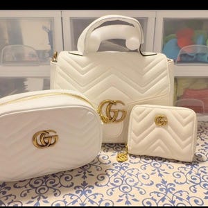 Puede incluir: Un conjunto de tres bolsos de cuero acolchado blanco con patr&oacute;n de chevr&oacute;n y herrajes dorados GG. La colecci&oacute;n incluye un bolso de mano con asa superior, un bolso bandolera redondeado y una peque&ntilde;a cartera con cremallera y logos dorados.