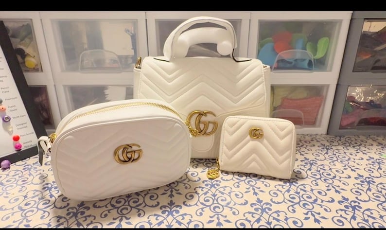 Puede incluir: Un conjunto de tres bolsos de cuero acolchado blanco con patr&oacute;n de chevr&oacute;n y herrajes dorados GG. La colecci&oacute;n incluye un bolso de mano con asa superior, un bolso bandolera redondeado y una peque&ntilde;a cartera con cremallera y logos dorados.