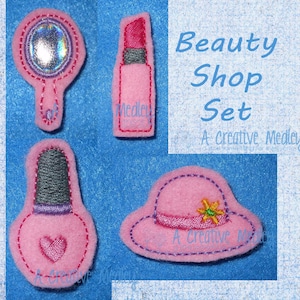 Puede incluir: Un conjunto de cuatro aplicaciones de fieltro para un tema de salón de belleza. El conjunto incluye un lápiz labial rosa, una botella de esmalte de uñas rosa con un corazón, un sombrero rosa con una flor verde y un espejo de mano rosa.