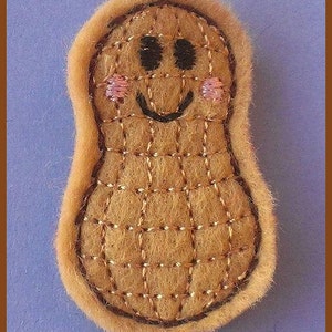 May include: A brown felt peanut with a smiling face, embroidered with black eyes and a mouth, and pink cheeks.