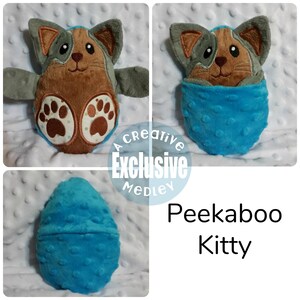 May include: A plush toy cat in a blue egg-shaped pouch. The cat has brown fur, gray ears, and black eyes. The pouch has a textured surface. The text "Peekaboo Kitty" is visible below the pouch.