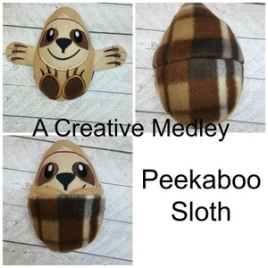 Puede incluir: Un juguete de peluche de perezoso marrón y beige con una barriga de tela a cuadros. El perezoso está asomando por la tela. El texto "Peekaboo Sloth" está escrito debajo de la imagen.