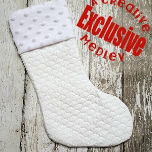 May include: White quilted Christmas stocking with a white plush top. The stocking has a scalloped design and is perfect for hanging on a fireplace mantel.