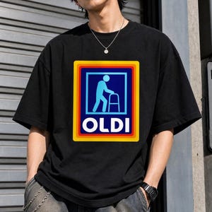 Peut inclure: T-shirt noir avec un logo parodique. Le logo présente une silhouette bleue utilisant un déambulateur dans un carré bleu, encadré de jaune, d'orange et de rouge. Le mot "OLDI" est en blanc. Vêtement décontracté.