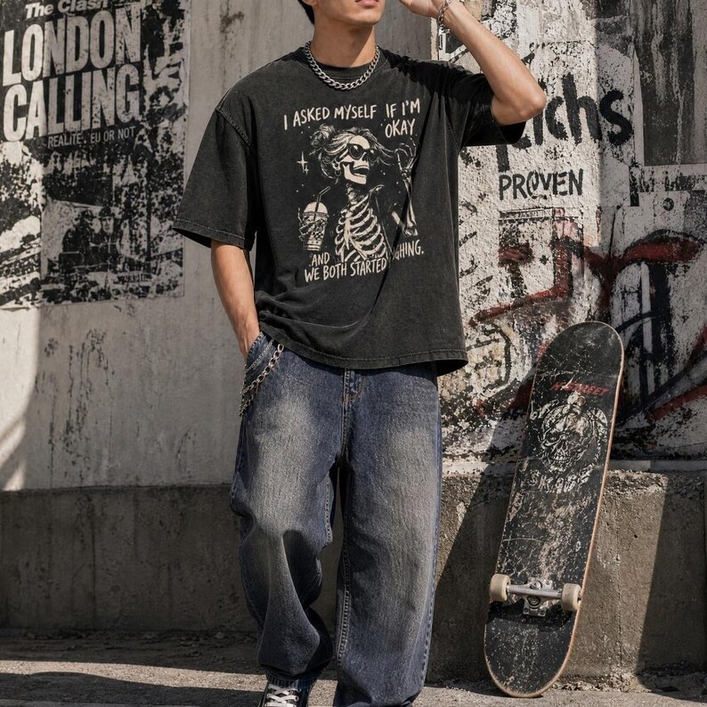 May include: A black graphic t-shirt with the text "I ASKED MYSELF IF I'M OKAY AND WE BOTH STARTED HING." The shirt is paired with blue jeans and a skateboard. The background features graffiti and posters.