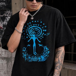 May include: Black t-shirt with a blue graphic depicting a figure with a halo and surrounding dots. Additional blue symbols and shapes are part of the design. The shirt has short sleeves and a loose fit.
