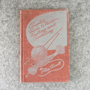 May include: A hardcover book titled Complete Guide to Modern Knitting and Crocheting by Alice Carroll. The cover is a textured reddish-orange fabric featuring a light gray graphic of a ball of yarn, two knitting needles, and a skein of yarn.