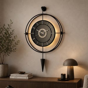 Op de afbeelding: Een grote, ronde wandklok met een zwart metalen frame en een donkergrijze wijzerplaat. De klok heeft een slinger en een gloeiend licht rond de wijzerplaat. De klok is bevestigd aan een lichtbeige muur.