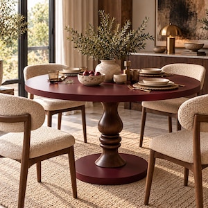 Può includere: Un tavolo da pranzo rotondo rosso scuro con una spessa base a piedistallo in legno scuro, circondato da quattro sedie con struttura in legno scuro e rivestimento testurizzato color crema. Il tavolo è apparecchiato con piatti, ciotole e bicchieri.