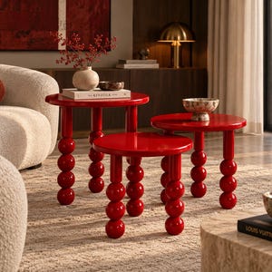 May include: A set of three round, glossy red side tables, each featuring three legs constructed from stacked spheres. The tables vary in height and are arranged in a cluster, showcasing a smooth, reflective surface and a vibrant, solid red finish.