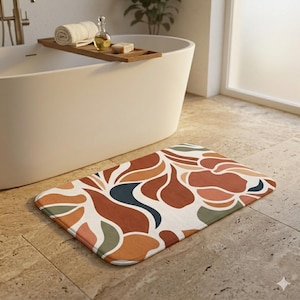 Può includere: Un tappetino da bagno rettangolare con un motivo floreale astratto nei toni del ruggine, arancione, verde e blu navy su sfondo bianco. Il tappetino è posizionato su un pavimento piastrellato davanti a una vasca da bagno bianca.