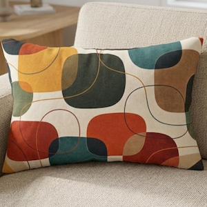 Pode incluir: Almofada retangular decorativa com fundo creme e um padrão geométrico colorido. O design apresenta formas sobrepostas em tons de laranja, verde-azulado, castanho, amarelo e verde escuro, com linhas curvas finas castanhas e pretas.