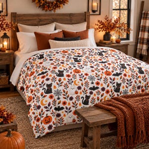 May include: A white bedspread featuring a repeating pattern of black cats, white ghosts, orange pumpkins, bats, spiderwebs, crescent moons, candy corn, and autumn leaves. The bedding is styled with several solid-colored pillows and a throw blanket.