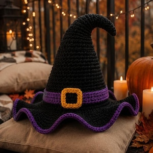 May include: A black crocheted witch hat featuring a purple band and a square yellow buckle. The hat has a pointed, slightly curved top and a wide, wavy brim with a purple crocheted edge, showcasing detailed yarn texture throughout the design.
