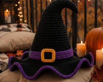 Puede incluir: Un sombrero de bruja de ganchillo negro con una banda morada y una hebilla cuadrada amarilla. El sombrero tiene una parte superior puntiaguda ligeramente curvada y un ala ancha y ondulada con un borde morado, mostrando una textura de hilo.