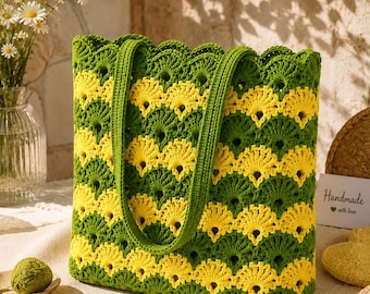 Puede incluir: Un bolso tote rectangular de ganchillo con un patrón repetitivo en forma de abanico en rayas horizontales alternas de hilo amarillo vibrante y verde oscuro. El bolso tiene dos asas de ganchillo verdes a juego y un borde superior festoneado.