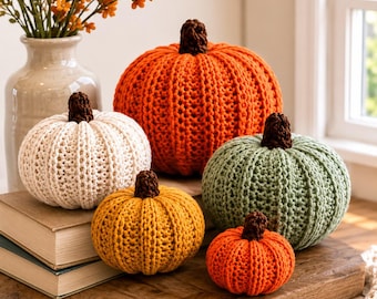 Puede incluir: Una colección de cinco calabazas de ganchillo de varios tamaños y colores, incluyendo naranja, blanco, verde salvia y amarillo mostaza. Cada calabaza presenta una textura acanalada y un pequeño tallo de ganchillo marrón oscuro.