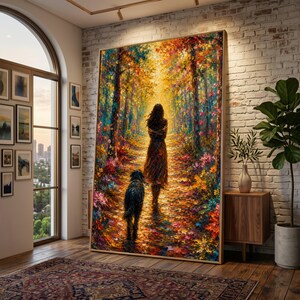 Könnte beinhalten: Ein großer, gerahmter Gemälde zeigt eine Frau und einen Hund auf einem Weg durch einen farbenfrohen Wald. Das Kunstwerk weist lebendige Farbtöne von Orange, Gelb und Grün auf und erzeugt eine warme Szene. Das Gemälde wird in einem gut beleuchteten Raum mit einer Backsteinmauer gezeigt.
