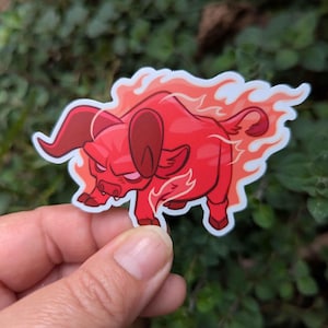 Puede incluir: Una pegatina roja con un toro de dibujos animados con llamas. El toro tiene una expresi&oacute;n feroz y est&aacute; caminando. La pegatina est&aacute; sobre un fondo de follaje verde.