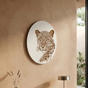 Puede incluir: Arte mural ovalado con un retrato detallado de un leopardo en tonos crema y marrón. La obra de arte está montada sobre un fondo color crema, creando un contraste llamativo. La cara del leopardo está intrincadamente diseñada, mostrando sus manchas.