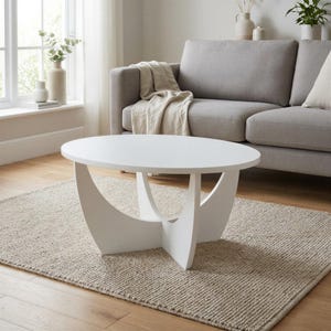 Pu&ograve; includere: Un tavolino da caff&egrave; ovale bianco con una superficie liscia, sostenuto da una base centrale composta da quattro pannelli curvi e intersecanti che creano una silhouette geometrica distinta, offrendo una base stabile al piano.