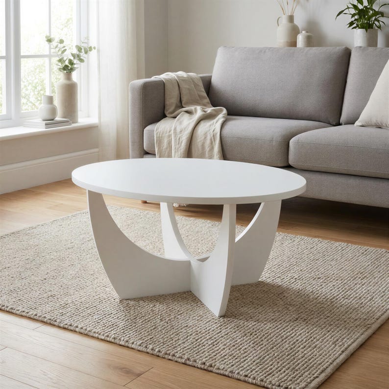 Pu&ograve; includere: Un tavolino da caff&egrave; ovale bianco con una superficie liscia, sostenuto da una base centrale composta da quattro pannelli curvi e intersecanti che creano una silhouette geometrica distinta, offrendo una base stabile al piano.