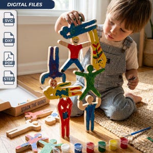 May include: A set of wooden human-shaped figures for stacking, featuring hand-painted designs in red, blue, green, and yellow. The set includes digital files labeled SVG, DXF, PDF, and STEP, with a cardboard box marked STACK THE DUDES.