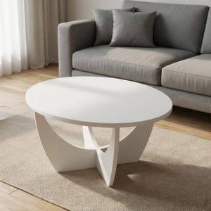 Pu&ograve; includere: Un tavolino da caff&egrave; bianco con un piano circolare liscio e una base composta da quattro pannelli curvi intersecanti che formano una struttura a croce. Il tavolo presenta una finitura bianca uniforme su tutta la sua superficie.