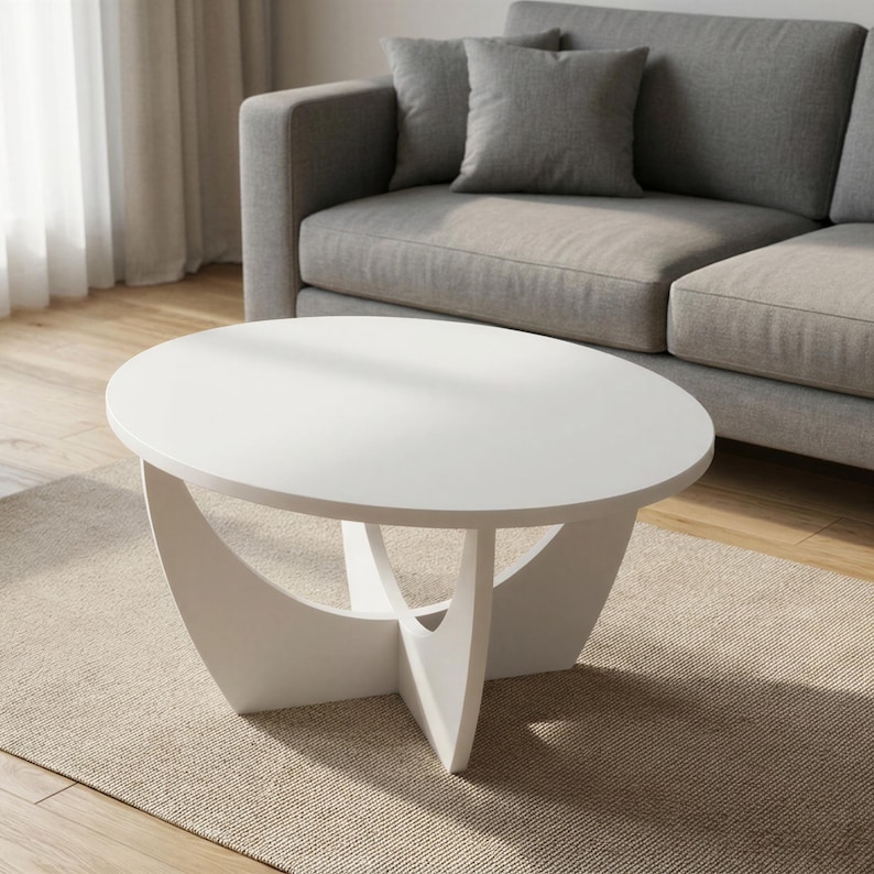 Pu&ograve; includere: Un tavolino da caff&egrave; bianco con un piano circolare liscio e una base composta da quattro pannelli curvi intersecanti che formano una struttura a croce. Il tavolo presenta una finitura bianca uniforme su tutta la sua superficie.