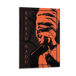 May include: A vertical rectangular wall art print featuring a high-contrast orange and black graphic illustration of a person wearing a headwrap. The text ERYKAH BADU is printed vertically in a serif font on the left side within a thin black border.