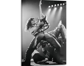 Puede incluir: Una fotografía en blanco y negro de un músico tocando una guitarra eléctrica a rayas en el escenario. El intérprete está inclinado hacia atrás con el pelo largo, mientras otro músico de pelo largo se ve al fondo cerca de una batería bajo luces.