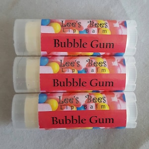 May include: Three lip balm tubes with a red, white, and yellow candy design. The label reads "Lee's Bees Lip Balm Bubble Gum".