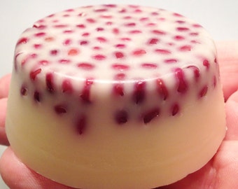 Puede incluir: Una pastilla de jabón redonda blanca con motas rojas. El jabón está en una mano.