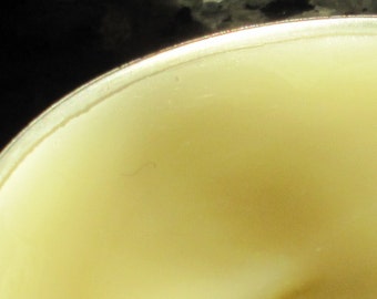 Puede incluir: Primer plano de un objeto redondo de color amarillo claro con un borde plateado. La superficie es lisa y parece ser de un solo color. El objeto está sobre un fondo oscuro y texturizado.