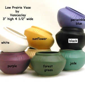 May include: Set of six low prairie vases by Veniceclay in various colors, including white, purple, forest green, jade, sunflower yellow, black, and periwinkle blue. Each vase is 3 inches high and 4 1/2 inches wide.
