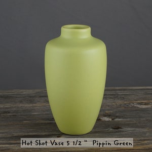 May include: A light green ceramic vase, 5 1/2 inches tall, with a rounded body and a narrow opening. The vase is labeled "Hot Shot Vase 5 1/2" Pippin Green".