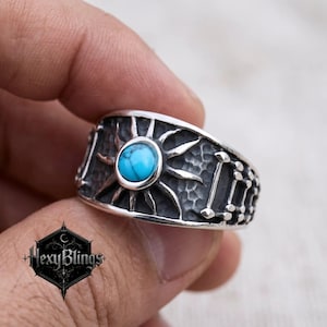 May include: A silver ring featuring a turquoise stone set in a sunburst design. The ring has a textured band with a series of vertical lines and dots. The ring is held in a hand.