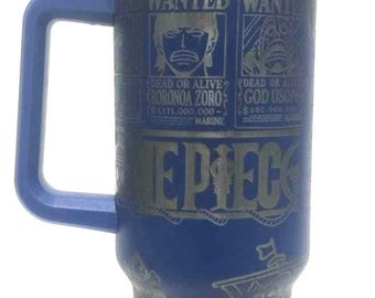 Puede incluir: Vaso azul con asa, con carteles de "WANTED" y texto "EPIEC". El diseño incluye imágenes de personajes y un barco. Tiene una tapa plateada y una pajita.