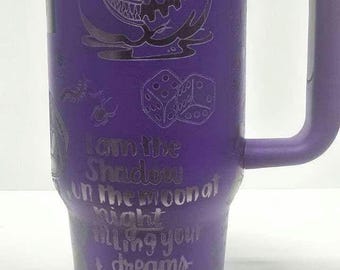 Puede incluir: Vaso térmico morado con asa, con diseños grabados con temática de Halloween. El vaso incluye una tapa y un asa. El texto en el vaso dice: "Soy la Sombra en la luna por la noche, llenando tus sueños hasta el borde de miedo."