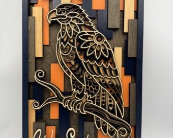 May include: A rectangular wooden wall art piece featuring a layered, laser-cut eagle perched on a branch. The background consists of vertical slats in navy blue, orange, and natural wood tones. The text "War Eagle" is displayed in white script.