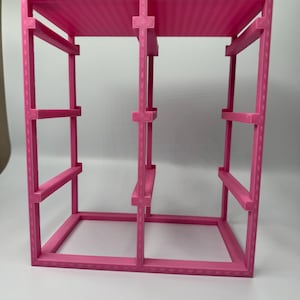 May include: A bright pink, rectangular, 3D-printed storage rack featuring a vertical frame with two main compartments. The structure includes a solid top panel and three horizontal support bars on each side, creating an open-grid design.