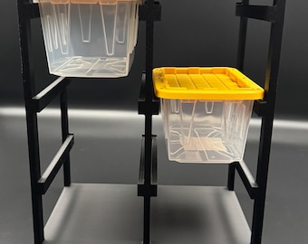 May include: A black storage rack with a grid frame featuring two clear plastic bins with yellow lids. The bins are suspended within the structure, one positioned in the upper left section and the other in the middle right section of the frame.