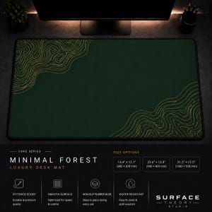 May include: A dark green Minimal Forest luxury desk mat with gold topographic design. The mat has stitched edges and a smooth surface. The text on the mat says "Surface Theory Studio". Available in 3 sizes: 14.4" x 12.1", 23.6" x 13.8", and 31.5" x 15.5".