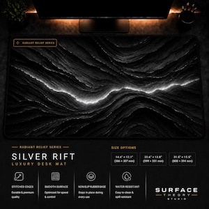 Op de afbeelding: Een rechthoekige bureaumat met een zwart-wit abstract ontwerp van een gloeiende kloof over een getextureerd landschap. De tekst luidt Radiant Relief Series, Silver Rift en vermeldt de afmetingen in millimeters.
