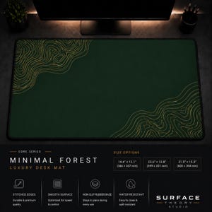 May include: A rectangular dark green desk mat featuring gold topographic line patterns in the top-left and bottom-right corners. The mat has black stitched edges and is labeled as Minimal Forest Luxury Desk Mat with size options of 14.4 x 12.1 inches, 23.6 x 13.8 inches, and 31.5 x 15.5 inches.